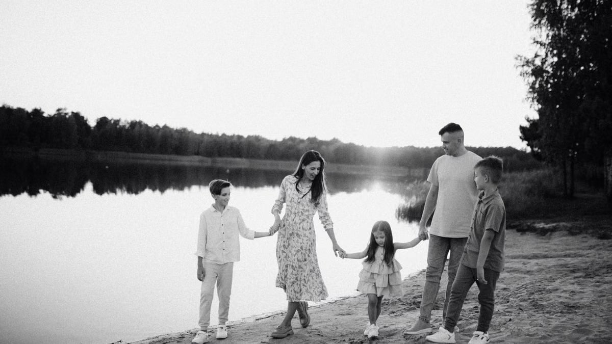 Monochrome photo of a family walking hand in hand along a serene lakeshore.